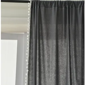 Detail of dark grey curtain fabric with decorative white pom-pom fringe and top folds