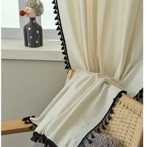 Detalle de cortina de lino y algodón beige con flecos decorativos de pompones negros