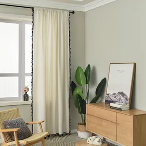 Detalle de cortina de lino beige con borlas negras en los bordes y montaje de barra