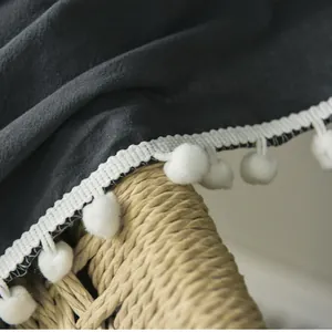 Close-up of dark grey linen curtain with decorative white pom-pom fringe edging