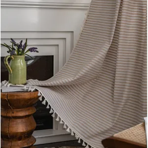 Striped linen curtain with white tassels displayed over a cozy fireplace and rustic decor