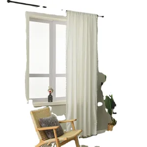 Minimalist white curtains with pom-pom fringe hanging on a black rod in a cozy bedroom