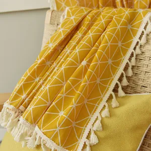 Detail of yellow geometric knit throw blanket with white tassels on a wicker chair