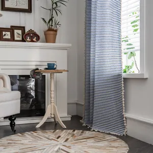 Detail of blue and white striped cotton linen curtain with cream tassels in cozy home setting