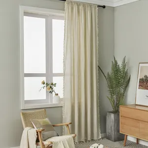Detail view of light beige linen curtain fabric featuring delicate fringe pom-pom trim