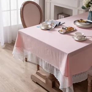 Detail van roze tafelkleed met witte kant kwastjes op een houten eettafel