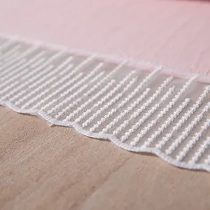 Detail van roze stof met witte golvende kantrand en verticaal geborduurd ontwerp