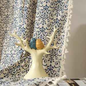 Artistic bird figurine on beige branch with vintage floral blue curtain background