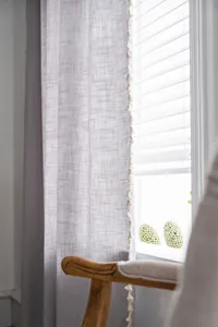 Detail of light grey linen curtain fabric featuring elegant white decorative tassels