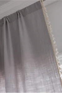 Detail of grey linen texture curtain with decorative cream tassels and fabric folds