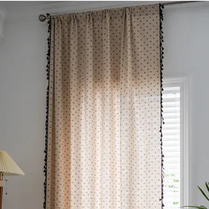 Close-up of beige cotton linen curtain with blue polka dots and black fringe tassels