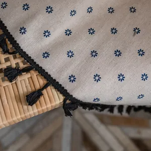Detail of blue daisy embroidery on beige linen fabric with black tassel fringe trim