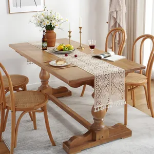 Detail of beige crochet table runner with lace patterns and tassel fringe on wooden table