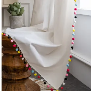 Detalle de cortina de estilo nórdico con flecos de pompones de colores y textura de lino
