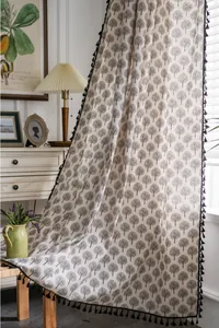Detail of beige curtain with black tree print and tassel trim in a cozy bedroom