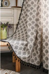 Detail of linen curtain with black tree patterns and fringe tassels in vintage setting