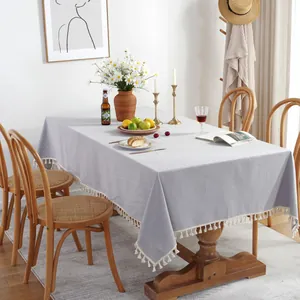 Nappe rectangulaire minimaliste en lin bleu clair avec pompons blancs sur table en bois