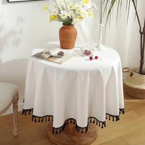 Detalle de mantel redondo de algodón y lino crema con elegantes flecos negros en el borde