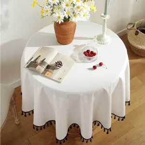 Mantel redondo minimalista de algodón y lino beige con borlas negras en la mesa