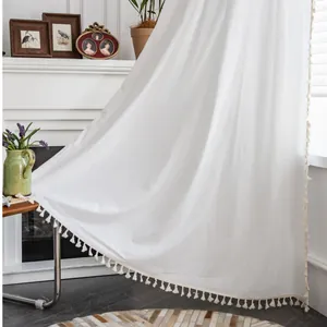 Dettaglio di tenda in cotone e lino bianco con nappe decorative e trama naturale