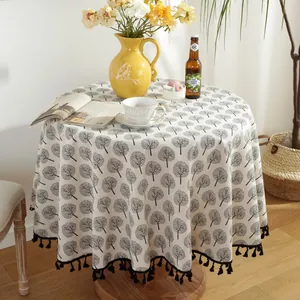 Macro detail of round cotton linen tablecloth featuring tree prints and black tassel fringe