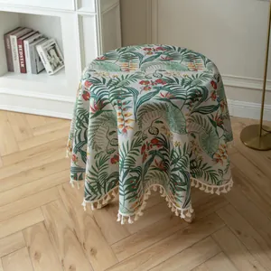 Dettaglio di tovaglia rotonda con stampa di piante tropicali e nappe bianche su pavimento