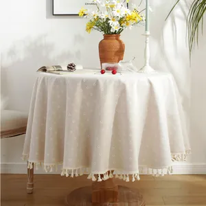 Detailed view of beige cotton linen round tablecloth with white floral pattern and tassels