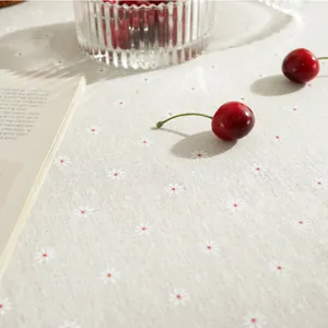 Detailed close-up of light beige cotton linen tablecloth featuring white daisy patterns