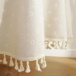 Detail of beige cotton linen tablecloth with white daisy prints and tassel fringe edge