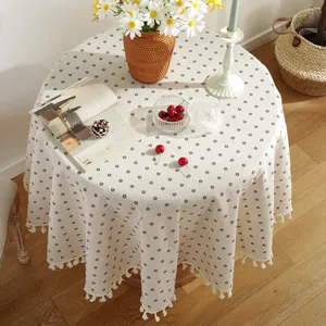 Detail of round linen tablecloth with daisy floral patterns and delicate white tassels