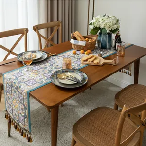 Gros plan d'un chemin de table bohème aux motifs floraux et pompons sur une table en bois
