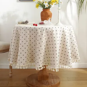 Detail of round beige tablecloth with coffee floral print and cotton fringe edges