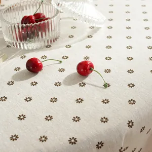 Detail view of beige linen tablecloth with daisy floral prints and red cherry decor
