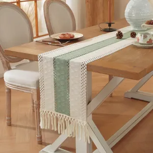 Detail van de saliegroene gebreide tafelloper met kwastjes op een houten tafel