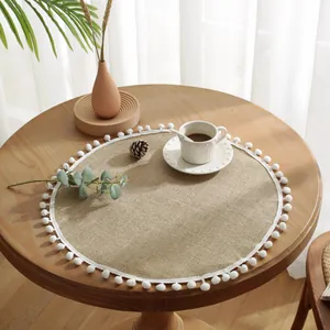 Nordisches rundes Jutetablett mit weißen Pompons auf einem rustikalen Holztisch