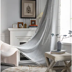 Detail of light gray plaid curtain with linen texture and white pom-pom tassel trim