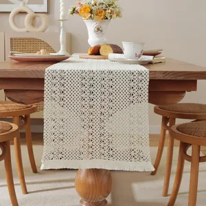 Detail of beige crochet table runner with geometric floral patterns and handmade tassels