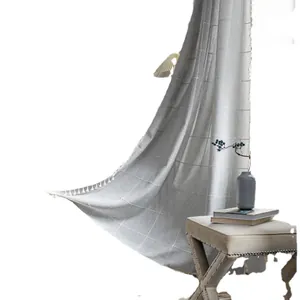 Grey plaid farmhouse curtain with white tassel trim displayed in a rustic interior setting