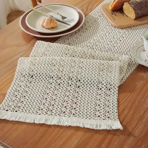 Close-up of cream crochet table runner with floral hollow patterns and tassel details