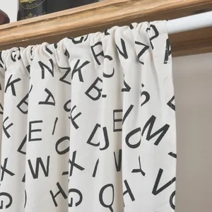 Detail der Leinengardine mit schwarzem Alphabet-Aufdruck und rustikaler Aufhängung