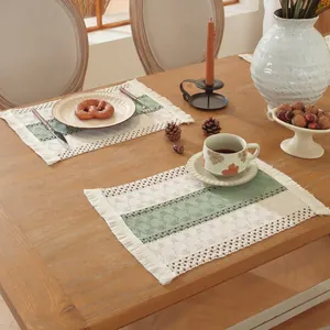Detalle de mantel individual tejido con toques verde salvia y borlas bohemias en madera