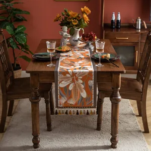 Détail d'un chemin de table jacquard orange avec motifs de feuilles et finitions pompons