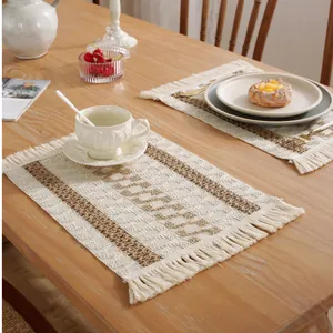 Detalle del mantel individual tejido beige con rayas marrones y flecos en madera