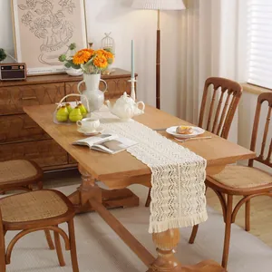 Beige crochet lace table runner with tassels and floral hollow pattern on a wooden table