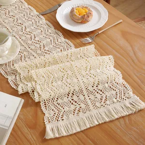 Beige crochet lace table runner with hollow floral patterns and fringe on wood desk