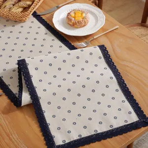 Détail du chemin de table en lin et coton à fleurs bleues avec larges bordures en dentelle