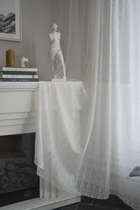 Detail of white hollowed-out lace curtain with Nordic clover pattern in a home setting