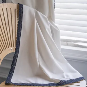 Modern minimalist cream linen curtain with dark blue lace trim hanging on a wooden chair