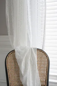Close-up of white lace curtain with intricate floral embroidery and scalloped edges