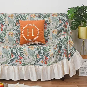Detail of tropical leaf sofa cover with cream ruffled hem and orange embroidered pillow